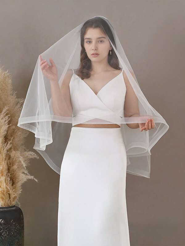 Ein einfacher zweischichtiger Brautschleier, kombiniert mit einem weißen Hochzeitskleid und Accessoires.