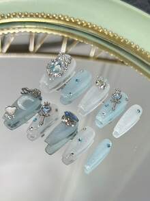 Bộ 10 móng giả hình quan tài dài, màu xanh dương lấp lánh, phong cách "Tinh khiết và quyến rũ". Móng giả dán phủ toàn bộ được trang trí bằng nơ đính đá, vòng hoa, đá hình trăng khuyết, đũa phép, đá hình trái tim và đá hình "trứng" màu xanh dương (thuật ngữ chỉ những viên đá lớn, bắt mắt) xếp chồng lên nhau. Dụng cụ làm móng, móng giả dán thủ công. - Nhiều màu - Xem 3