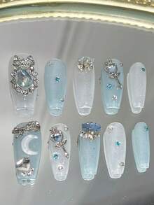 Bộ 10 móng giả hình quan tài dài, màu xanh dương lấp lánh, phong cách "Tinh khiết và quyến rũ". Móng giả dán phủ toàn bộ được trang trí bằng nơ đính đá, vòng hoa, đá hình trăng khuyết, đũa phép, đá hình trái tim và đá hình "trứng" màu xanh dương (thuật ngữ chỉ những viên đá lớn, bắt mắt) xếp chồng lên nhau. Dụng cụ làm móng, móng giả dán thủ công. - Nhiều màu - Xem 1