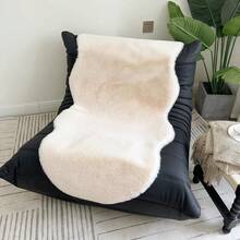 1件仿毛皮米色不对称造型沙发垫，可用作床边垫、躺椅垫。毛绒柔软，高密度聚酯纤维填充。适用于客厅沙发、床边等多种场所。