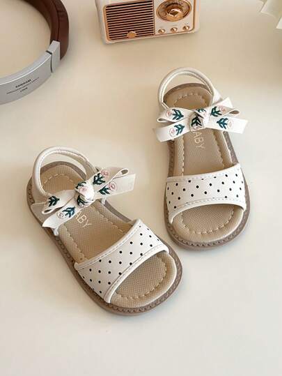这款女童凉鞋采用波点和蝴蝶结花朵设计，PU皮革材质，舒适防滑，露趾低帮，魔术贴搭扣，平底款式，甜美田园风凉鞋，适合日常街头穿着和夏季休闲活动。
