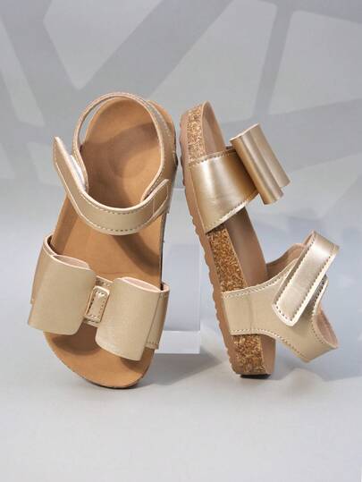 1 đôi sandal hở mũi cho bé gái, trang trí nơ vàng, làm từ chất liệu PU mềm mại, thiết kế cổ thấp có quai, kiểu dáng đế bằng với các chi tiết lấp lánh vàng tinh tế, phù hợp cho cả mặc hàng ngày và các dịp cưới hỏi.