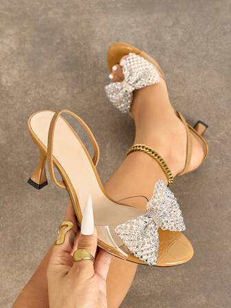Women's High Heel Shoes, Fashionable And Elegant For Parties, Outdoor Events, And Formal Occasions. Features Include: Stiletto Heel, Round Toe, Sparkling Rhinestones, Oversized Bow Accent, PVC Transparent Glass-Like Material, Textured Stone-Like Pattern, Ankle Strap, Versatile And Suitable For Dresses. Available In Camel Color.