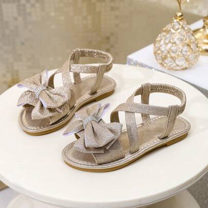 一双儿童夏季新款时尚平底凉鞋，饰有大蝴蝶结和交叉绑带设计，可爱俏皮，适合女孩户外、旅行、海滩度假穿着。