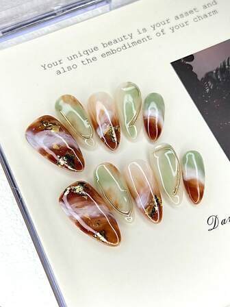 10 st. mitten ovala press-on naglar med brun-grön agatstruktur, gradienttonade premium lyxiga baser, bladguldelement och metallnålsdekoration. Glänsande 100 % handgjorda press-on akrylnaglar. Återanvändbara nageltillbehör för kvinnors vardags- eller festkläder.