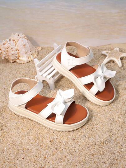 一双女童鞋，白色蝴蝶结双带设计，后跟带袢。鞋面采用人造革材质，饰有立体蝴蝶结，低帮露趾设计。厚底舒适，甜美公主风，适合生日派对和儿童节表演等场合。