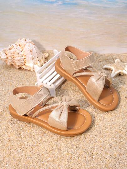 1 Pair Of Girls' Shoes With Light Gold Bow Cross Strap Sandals, The Upper Is Made Of Shiny Material, Decorated With Bow Ties, And Features A Low Cut Design With Exposed Toes. The Flat Bottom Is Comfortable, Gentle And Fairy Like, Suitable For Beach Vacations And Birthday Parties