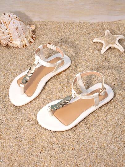 一双女童鞋，白色金属夹扣平底凉鞋，鞋面饰有金属装饰，露趾款式。平底柔软时尚，适合假日家庭短途旅行和海滩玩耍。