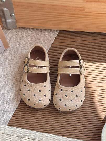 Dessa flickskor är tillverkade av ljusbeige prickigt tyg, i kombination med matchande dubbelspännedesign, vilket visar upp en söt och lekfull stil. Innersulan är dekorerad med märkets logotyp.