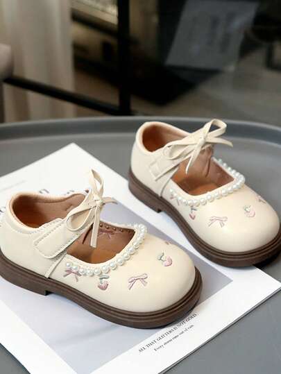 1双米色轻便透气休闲平底鞋，适合幼儿和小女孩穿着。鞋面采用简约优质的PU材质，饰以水果刺绣、蝴蝶结和珍珠吊坠，洛丽塔风格，舒适的弹性内衬，耐磨厚橡胶鞋底，魔术贴设计，适合搭配公主裙、日常穿着、上学、外出、派对、度假等场合，2026春夏款。
