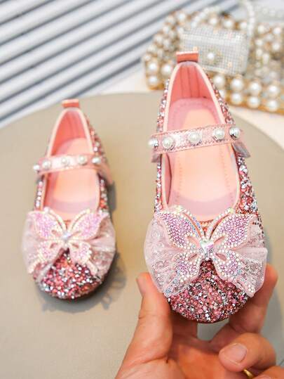 1双女童亮片平底鞋，采用闪亮PU材质，镶嵌水钻和珍珠蝴蝶结，闭趾设计，适合派对、舞蹈和日常穿着。