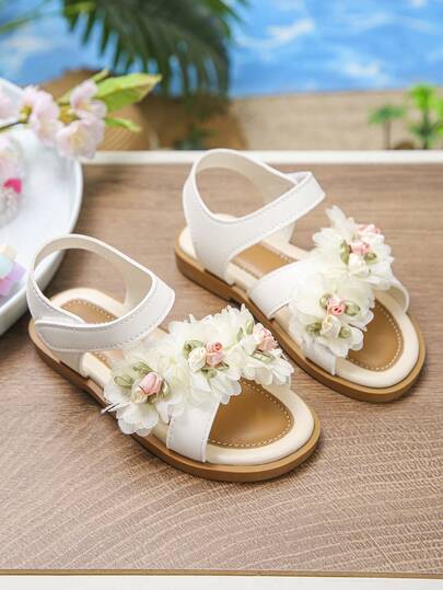 Giày sandal đế bằng hoa trắng mới cho bé gái mùa xuân/hè 2026, kiểu công chúa với hoa 3D bằng sợi len, đế mềm mại, thoải mái, giày La Mã đa năng cho trẻ em.