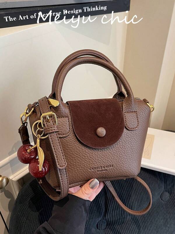 Esta bolsa feminina é feita de couro PU quadrado na cor café, combinando estética e estilo versátil. Possui zíperes de metal suaves, duas alças superiores, decoração com letras e um pingente de cereja vermelha. O corpo da bolsa tem uma textura granulada e uma alça de ombro longa e ajustável para facilitar o transporte.