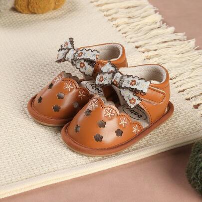 Ett par flickskor med broderad rosett och kardborreknäppning, söta blommiga platta sandaler lämpliga för sommarens bohemiska stil, som present till en bankett eller fest.