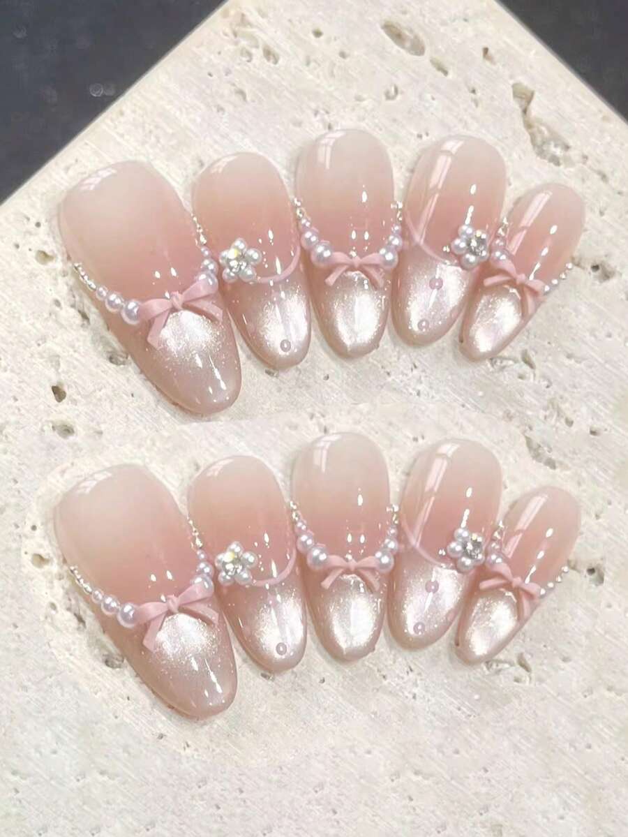 10片纯手工制作的长款椭圆形美甲贴片，底色为裸粉色，搭配香槟色猫眼法式风格。饰有粉色立体蝴蝶结、珍珠链、小水钻和手绘波点，呈现精致甜美的风格。温柔优雅的可爱美甲，适合女士和女孩在春夏秋冬各种节日、派对和日常生活中使用。 - 粉色 - 查看 1