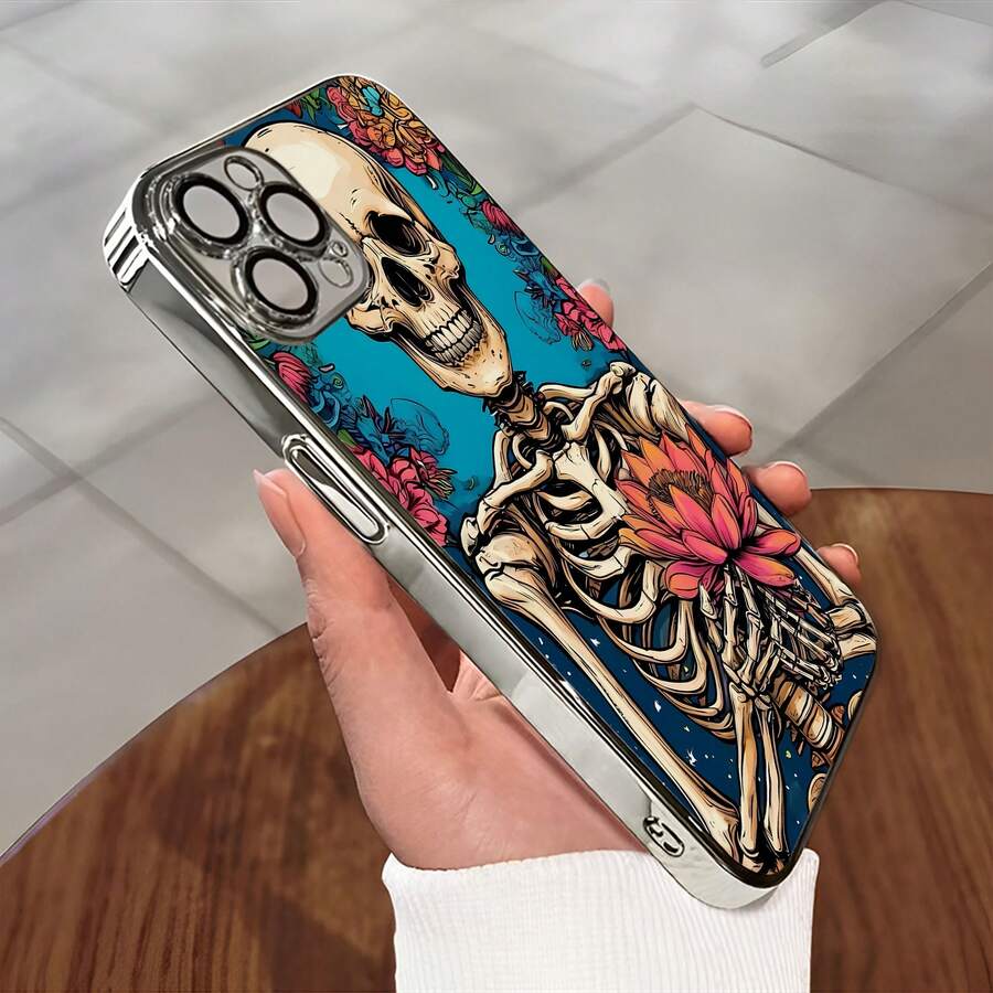 Esqueleto sonriente sosteniendo una flor rodeado de un diseño floral. Esta elegante funda es compatible con los modelos  17, 16, 15, 14 Pro Max, 13, 12, 11, XR y XS Plus. Fabricada en silicona TPU, ofrece protección contra golpes y caídas, además de una sensación superior. Es un regalo ideal para familiares, amigos y seres queridos, y una opción perfecta para Año Nuevo. - Plateado - Ver 1
