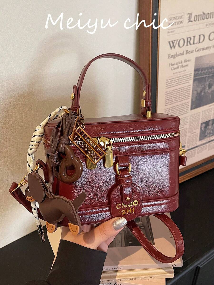 这款时尚的酒红色女士PU皮手提包款式多样，实用性强。包身饰有腊肠犬、饼干和算盘等可爱挂件。这款方形手提包配有字母标签，采用高品质五金配件，并配有顺滑的拉链。