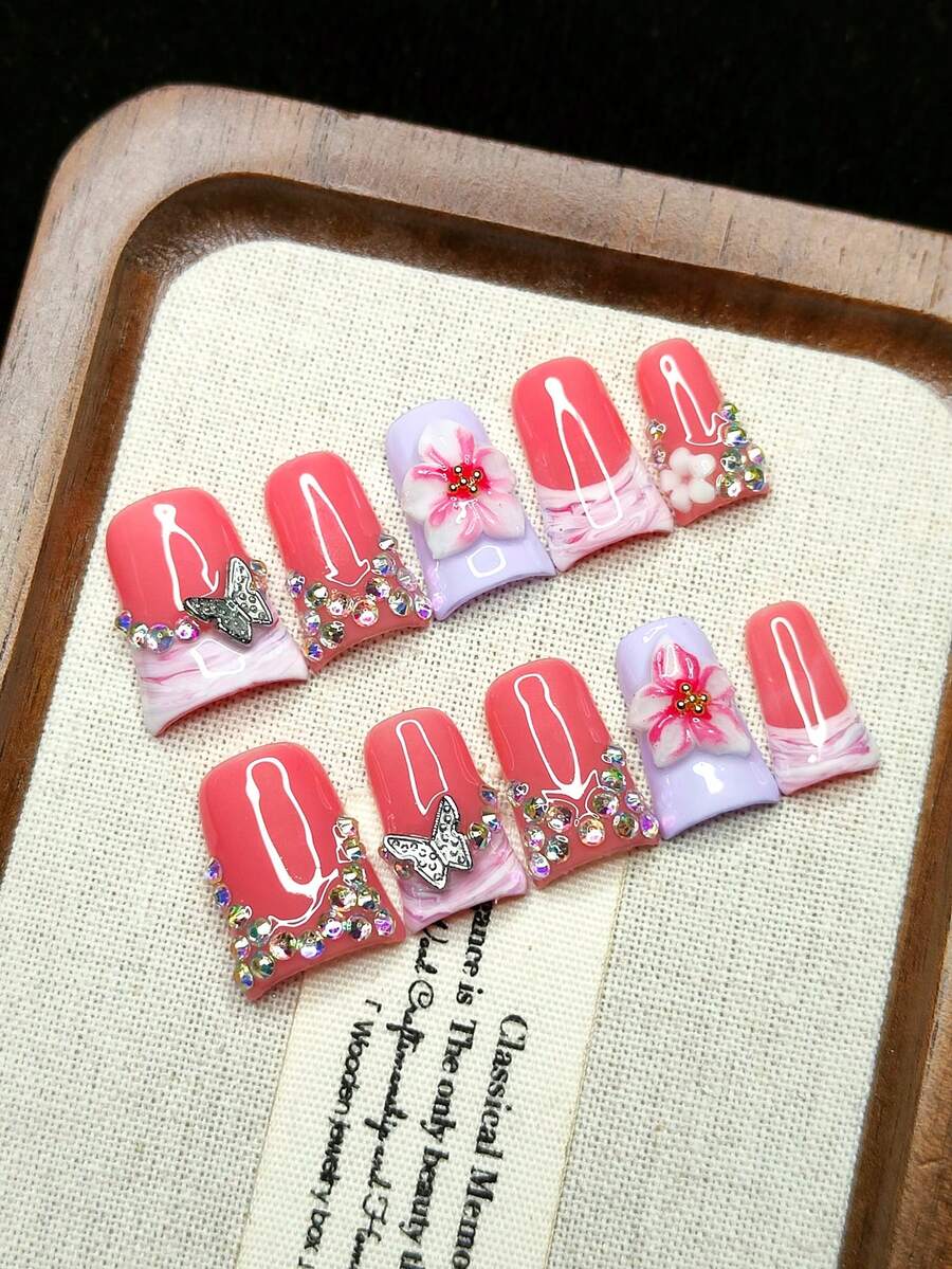 10片/套 手工按压式人造指甲。鸭嘴造型，色彩鲜艳亮丽，粉色底色搭配白色3D立体花朵装饰和精致金属蝴蝶点缀。个性十足的少女风。可重复使用。