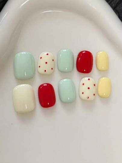 10 piezas de uñas postizas de corta longitud y forma ovalada hechas a mano. Los tonos principales son verde menta, amarillo crema y blanco crema, que pertenecen a la serie de colores macaron de baja saturación. Están complementados por acentos brillantes y llamativos en rojo brillante. En el blanco crema, hay pequeños elementos de lunares rojos. Suministros de uñas