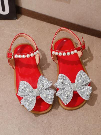 زوج من صنادل صيفية مسطحة للبنات، بتصميم عصري باللون الأحمر، برؤوس مستديرة مفتوحة، إغلاق بخطاف وحلقة، مزينة بفيونكة من البلورات والخرز، مناسبة للارتداء في المدرسة والاستخدام اليومي