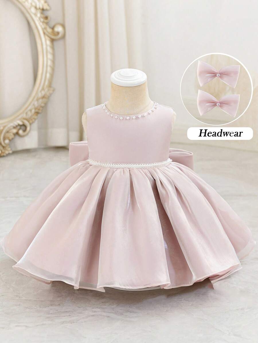 Đầm mini không tay cổ tròn màu hồng cho bé gái, chất liệu organza, đính hạt cườm và có nơ phía sau, kiểu dáng công chúa thanh lịch, thích hợp làm phù dâu trong đám cưới, dự tiệc sinh nhật, tiệc chiêu đãi, dạ hội.