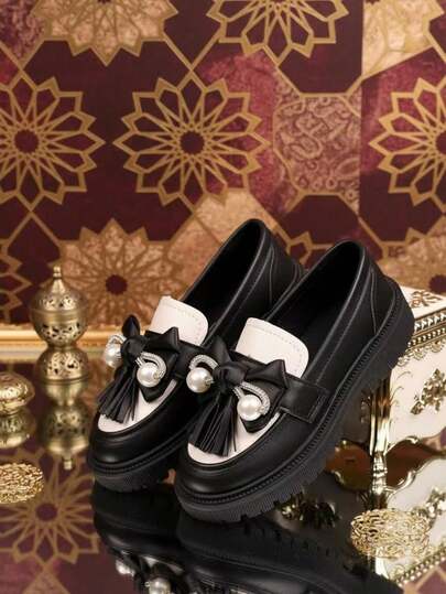 一双儿童鞋，黑白经典设计，厚底，饰以蝴蝶结和珍珠，精致可爱，展现童真与优雅。采用优质皮革制成，舒适透气，适合日常穿着、户外活动或派对场合，易于搭配各种服饰。