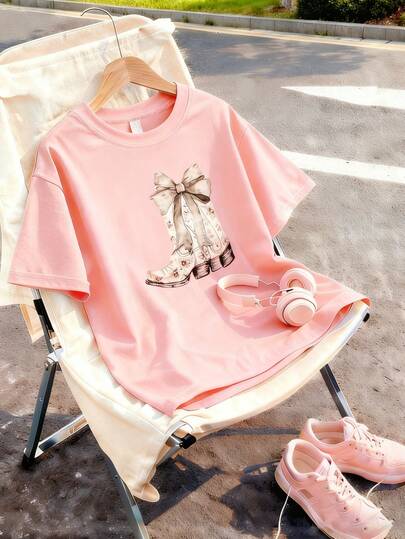 Esta camiseta de manga corta para niñas presenta un diseño único de estampado de zapato con lazo y un cuello redondo suave, convirtiéndola en una camiseta rosa casual
