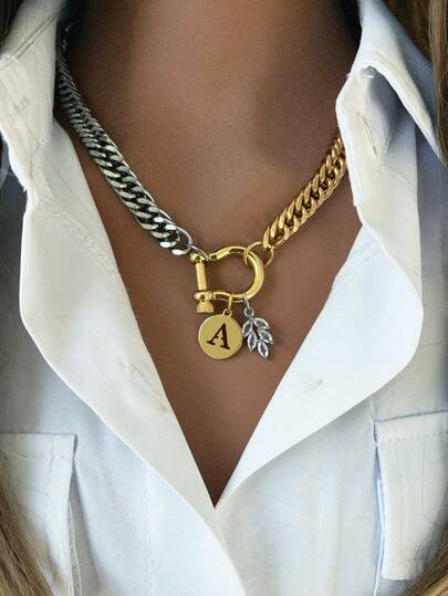 这款时尚双色女士项链，一端是粗金链，另一端是粗银链，两端通过一个闪亮的金色马蹄形搭扣连接。项链配有两个吊坠：一个可定制的圆形字母吊坠（字母可选），以及一个精致的银叶吊坠。这款项链兼具个性与时尚，适合日常佩戴或出席派对等场合。