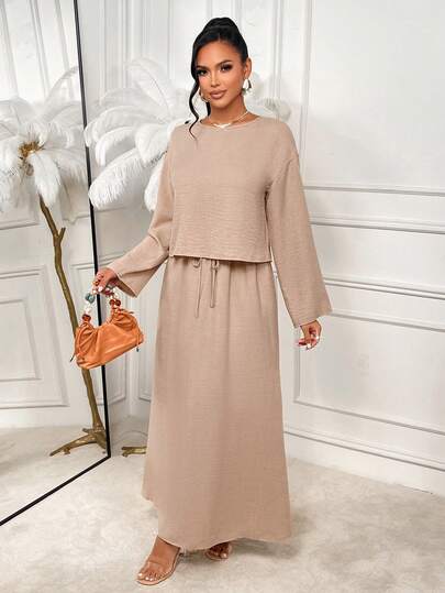 AIJ 这款来自 Amarilo 的卡其色纹理两件套，为您带来极致舒适与时尚体验。套装包含一件宽松长袖露脐上衣和一条高腰抽绳长裙，专为轻松日常穿着而设计。轻盈的纹理面料确保夏季透气舒适，宽松的版型则带来全天候的舒适感——无论是度假休闲、居家放松，还是作为斋月期间的得体装扮，都是理想之选。搭配凉鞋和斜挎包，打造休闲时尚造型。