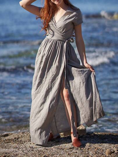 Plus Size Women's Solid Color Linen Maxi Dress, V-Neck Criss-Cross Design Elegant & Slimming, Loose Fit Accommodates Various Figures. The Flowing Hem Of The Dress Blowing In The Wind On The Rocky Beach Showcases The Beauty Of Natural Movement. Lightweight Breathable Fabric Suitable For Summer Vacation Wear