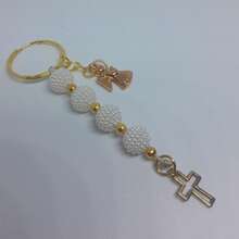 Set de 6/12 piezas. Llavero de perlas texturizadas con ángel y cruz ✨  Hermoso llavero elaborado con cuentas blancas texturizadas tipo perla y detalles en esferas metálicas doradas. Incluye dije colgante en forma de cruz y figura de ángel en tono dorado, aportando un diseño delicado y elegante.  Ideal como recuerdo para bautizo, primera comunión, confirmación, boda o eventos especiales. Perfecto para obsequiar a invitados o incluir en sets para celebraciones.  ✔ Diseño elegante en blanco y dorado ✔ Ligero y práctico ✔ Detalles decorativos metálicos ✔ Ideal para recuerdo de evento - Ver 2