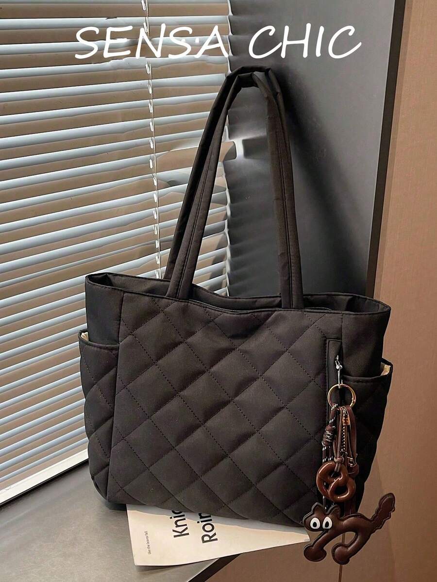 Chiếc túi xách nữ này được làm từ vải polyester màu đen tuyền với thiết kế chần bông, và được trang trí bằng một mặt dây chuyền hình gấu nhỏ. Túi có ngăn đựng cốc ở cả hai bên và khóa kéo kim loại ở phía trên.