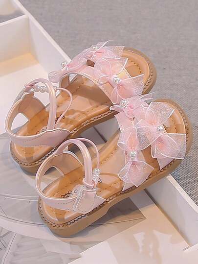 这款儿童平底凉鞋采用柔和的粉色调，饰以闪亮的多层蝴蝶结和圆润的珍珠，散发着梦幻公主般的气息，是搭配连衣裙的理想之选。鞋面采用亲肤人造革，内衬透气舒适。环绕式踝带设计方便穿脱，确保穿着稳固。防滑橡胶外底带有纹路，增强玩耍时的稳定性。脚踝处点缀着精致的珍珠链，增添优雅活泼的细节。