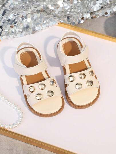 1双米色儿童平底凉鞋，撞色软PU鞋面，金属珠饰，搭扣设计，柔软鞋垫，舒适简约圆头防滑设计，可爱罗马风沙滩凉鞋，适合3-15岁女孩，适合沙滩、日常、休闲、派对等场合，春夏新品。
