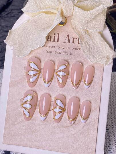 10片手工制作杏仁形白色法式假指甲，饰以金色三瓣花边。纯手工制作的白色法式风格，点缀金色闪粉和3D线条，手工绘制3D金色三瓣花边和金色法式轮廓。优雅、浪漫、简约的按压式美甲贴片，奢华、性感、轻盈。适合日常佩戴、约会、音乐会和轻度商务场合。是送给女性和女孩的理想礼物。