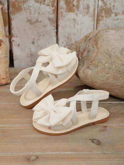 1 Pair Beige Infant/Toddler Girls' Flat Sandals, Solid Color Soft Fabric Criss-Cross Strap With Bow Decor, Classic Round Toe Open Toe Non-Slip Slip-On Design, Fashionable Cute Princess Style Beach/Casual Sandals For Spring/Summer