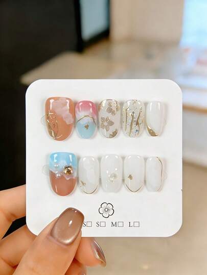 10片手工制作的按压式假指甲，短款杏仁形，渐变美甲，金色镜面粉花朵图案，不规则线条和美甲水钻点缀。这些精美可爱的指甲贴片可重复使用，易于粘贴和卸除，优雅的美甲装饰适合女孩和女士日常佩戴，也适合派对、婚礼和节日等场合。套装包含果冻胶、指甲锉和其他美甲配件。