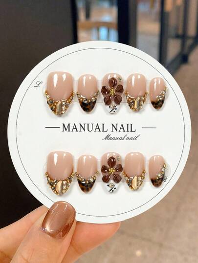 JUTI 10 Handmade Short Almond-Shaped Press-On Nail Stickers, In Nude Pink With A Glossy Finish For A Bold, Eye-Catching Look, Featuring A Sharp-Tip Design. They're Accented With Hand-Carved 3D Brown Flowers, Hand-Drawn Leopard Print, Gold And Crystal Decorations, Showcasing These Edgy Glamorous Nails.