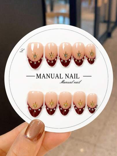 JUTI 10 Handmade Short Almond-Shaped Press-On Nail Stickers, Featuring A Classic Romantic Contrast Of Nude Base With Hand-Drawn Gold Starburst And Sparkling Rhinestone Accents, Accented With Burgundy Red French Tip Tips. They Are 100% Hand-Painted And Handcrafted, Showcasing These Elegant Festive Glamorous Nails. Characterized By A Timeless, Stylish, And High-Quality Aesthetic, These Nails Suit Both Mature And Youthful Styles, Work For Any Occasion, And Are Easy-To-Remove Press-On Nail Stickers.