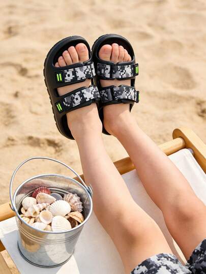 这款男童鞋采用浅灰色轻质橡胶和塑料鞋底，双绑带设计，鞋带饰有蓝、白、灰像素迷彩图案，搭配荧光绿/白色装饰扣，以及防滑纹理鞋底。露趾凉鞋款式融合了运动与时尚元素，适合2026年夏季室内、室外休闲穿着以及轻度运动。