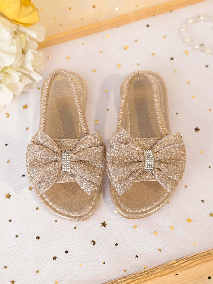 1 đôi sandal đế bằng màu vàng kim cỡ lớn dành cho bé gái, chất liệu PU mềm mại, bóng bẩy, trang trí nơ lớn, quai đeo mắt cá chân co giãn, mũi tròn, đế chống trượt thoải mái, kiểu sandal La Mã thời trang, thanh lịch, dễ thương phù hợp cho bé gái từ 3-15 tuổi, dùng hàng ngày, dự tiệc, du lịch, mùa xuân/hè 2026. - Hoa hồng vàng - Xem 1