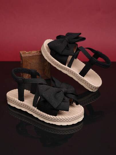 1 par de sandalias planas negras para niñas pequeñas/de talla grande, con tira de tela suave sólida con decoración de lazo, diseño de tira cruzada elástica de una sola tira, punta redonda abierta, cómodas y lindas sandalias romanas, adecuadas para niñas de 3 a 15 años, para uso diario, viajes, vacaciones, primavera/verano