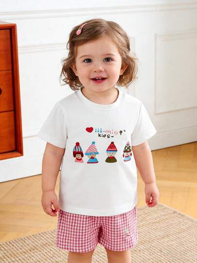 女婴可爱卡通套装：白色短袖T恤，印有“Mio!Baby Girl”字样和彩色图案；粉白格纹短裤，饰有草莓刺绣；面料柔软透气；可爱的图案和格纹元素，适合夏季穿着，舒适易搭，日常百搭。