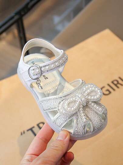 1 Đôi giày công chúa thời trang mùa hè mới cho bé gái, làm thủ công với đá pha lê và ngọc trai, có nơ buộc và trang trí pha lê, thích hợp cho trẻ sơ sinh và trẻ nhỏ tham gia các hoạt động ngoài trời, dự tiệc và nhiều dịp khác nhau.