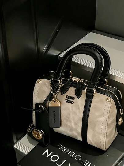 这款时尚新款女士半软摩卡色枕形包采用PU材质，配有可拆卸肩带，并饰有金属吊饰和标签。它是一款优雅的女士手提包/单肩/斜挎包，质感高端，适合通勤、聚会和购物等场合。