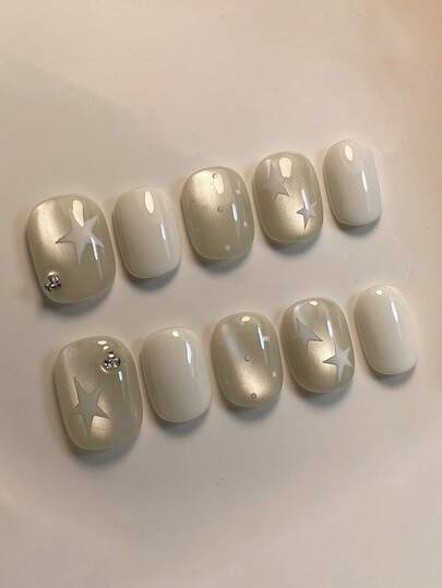 10片纯手工按压式美甲贴片，短款椭圆形美甲贴片，白色美甲贴片，简约可爱风格，搭配香槟色猫眼手绘星形图案和水钻装饰，温柔梦幻的按压式美甲贴片，适合女性和女孩，春夏秋冬节日派对及日常生活使用。