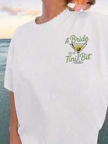 Camiseta Gráfica Oversized para Mujer 100% Algodón - Blanca, de Manga Corta, con Texto Divertido "A Bride In A Tini Bit" y Estampado de Copa de Martini. Top de algodón suave de corte holgado, perfecto para despedidas de soltera, fiestas de novias, viajes de chicas y eventos previos al matrimonio. Camiseta popular con temática nupcial, de corte cómodo y relajado, ideal para futuras novias y miembros del cortejo nupcial. - Blanco - Ver 2