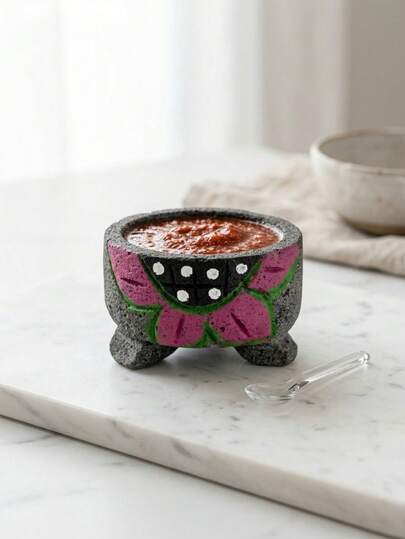 Cuerpo redondo, textura rugosa, patas cortas, decoración pintada. Este molcajete es perfecto para la preparación de salsas, guacamole, especias o servir alimentos en reuniones familiares, fiestas tradicionales, celebraciones mexicanas y convivios donde se quiera aportar un toque auténtico a la mesa.