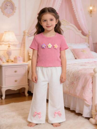 Bộ đồ mùa hè mới ngọt ngào và năng động cho bé gái, gồm áo thun ngắn tay rộng rãi, thoáng khí với chất liệu vải dệt họa tiết, kết hợp cùng quần ống rộng cạp chun, điểm nhấn là nơ hồng, thời trang và đa năng cho bé mặc hàng ngày.