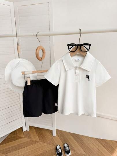 Bộ 3 món đồ mặc thường ngày mùa hè cho bé trai: Áo polo trắng thêu họa tiết đen, quần short đen và mũ tai bèo trắng, thích hợp cho dạo phố, đi học và mặc hàng ngày.